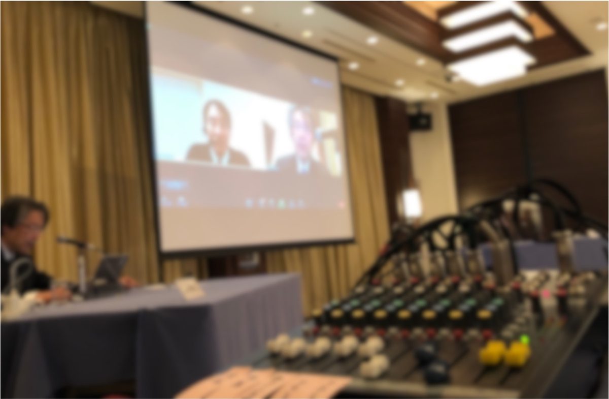 ホテル広間での学会配信。スクリーンにリモート発表者が映る